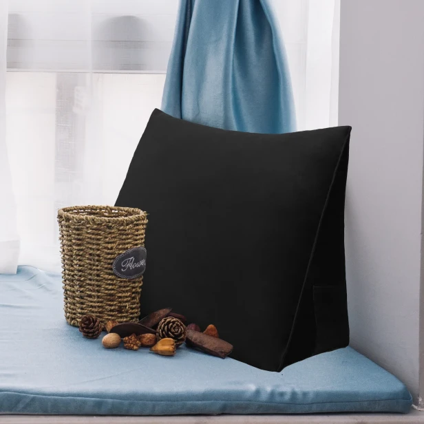 Auf einer gemütlich arrangierten Fensterbank liegt ein schwarzes Keilkissen – perfekt zum Lesen.