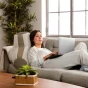 Eine junge Frau liegt bequem auf einem Sofa und lehnt sich an ein ergonomisches Rückenkissen in Wellenform.