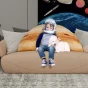 Ein entzückendes Foto von einem Kind mit Astronautenhelm und einem weißen Hund, der auf einem beigen Sofa mit einem riesigen 3D-Jupiter-Kissen sitzt.
