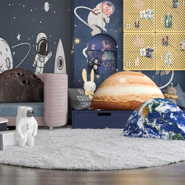 Ein aufwendig dekoriertes Kinderzimmer in Marineblau und Gelb mit drei großen Kissen, die die Planeten Jupiter, Erde und Mond zeigen. Die Tapete im Hintergrund zeigt einen Astronauten und eine Rakete.