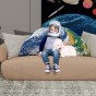 Ein kleines Kind mit Astronautenhelm sitzt auf einem großen, halbkreisförmigen Kissen mit einem 3D-Druck des Planeten Erde.