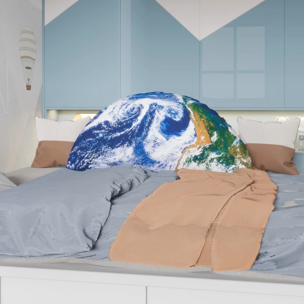 Ein großes, dekoratives Kissen in Form einer Halbkugel mit einem Aufdruck des Planeten Erde, platziert auf einem Bett mit blauer und beiger Bettwäsche.