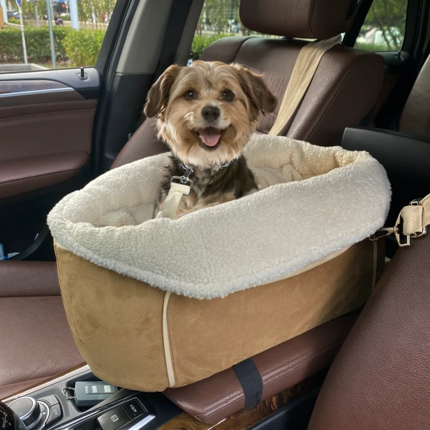 Ein kleiner, glücklicher Hund sitzt in einem beigen Autositz, daneben eine Hundetragetasche für die Armlehne mit cremefarbenem, flauschigem Bezug.