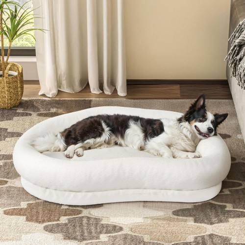 Ein Hund liegt bequem in einem großen, ovalen Cloud-Hundebett in hellbeige.