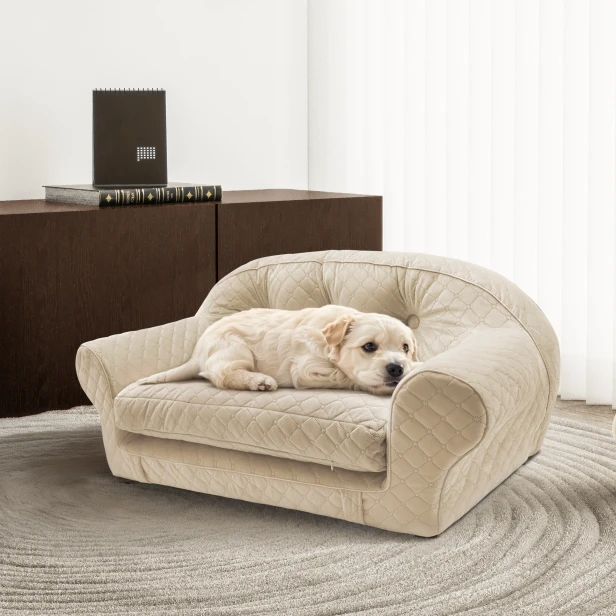 Ein Welpe liegt auf einem luxuriösen, beigefarbenen, gesteppten Hundesofa in einem eleganten Interieur.