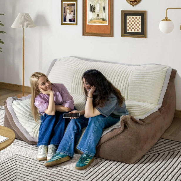 Zwei junge Frauen sitzen auf einem großen, modularen, braunen Lounge-Sofa mit beigefarbenem Steppbezug.