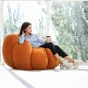 Frau sitzt mit einer Tasse Kaffee auf einem kürbisförmigen Pouf.