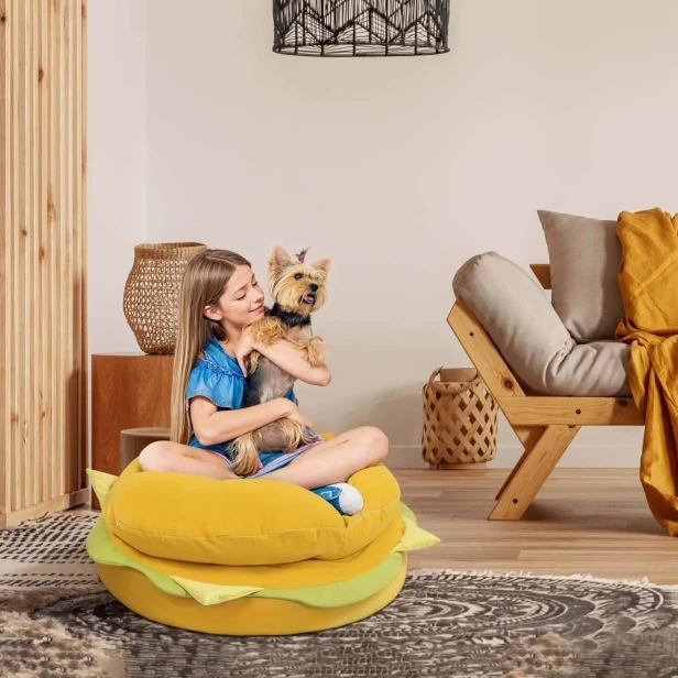 Ein junges Mädchen sitzt in türkischer Position auf einem großen, runden Hamburger-Pouf, der als bequemer Sitzplatz auf dem Boden dient.
