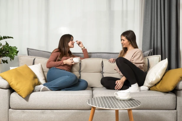 Zwei Frauen lehnen an einem Sofa mit beigefarbener und grauer Kopfstütze mit Stauraumkissen.