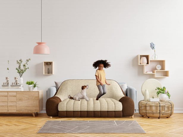 Kind springt mit Hund auf dem Komfortsofa, Arrangement im Wohnzimmer.