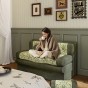 Eine Frau sitzt mit einem Laptop auf dem Schoß auf einem Zweisitzer-Sofa.
