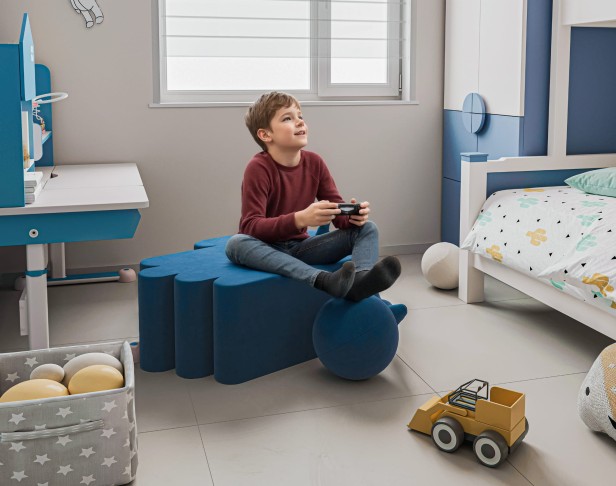 Junge sitzt und spielt auf einem modernen blauen Pouf.