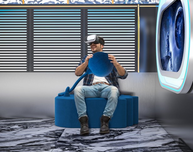 Mann sitzt und spielt auf einem modernen blauen Pouf.