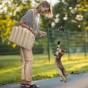 Frau spielt mit Katze im Park, luxuriöse Haustiertasche über der Schulter.