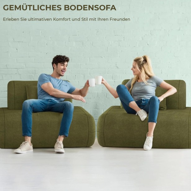 Ein junges Paar sitzt auf zwei Elementen eines bequemen olivgrünen Sofas und stößt mit Tassen an. Das Foto vermittelt Stil und Gemütlichkeit unter Freunden.