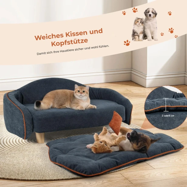 Die Katze liegt auf einem eleganten, grauen Sofa und benutzt die weiche Kopfstütze (Rückenlehne), und daneben, auf dem Boden, spielt ein Welpe vergnügt auf einer herausgenommenen Matratze.