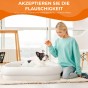 Eine Frau kniet neben einer französischen Bulldogge, die in einem flauschigen weißen Bett liegt.