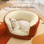 Die weiße Katze liegt gemütlich in einem weichen, terrakottafarbenen und beigen Bett mit hohem Rand.