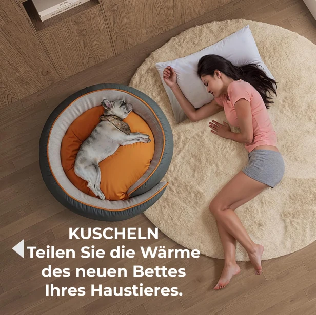 Der Hund schläft zusammengerollt in einem warmen, runden Bett in Grau und Orange, während die Frau neben ihm auf dem Teppich schläft.