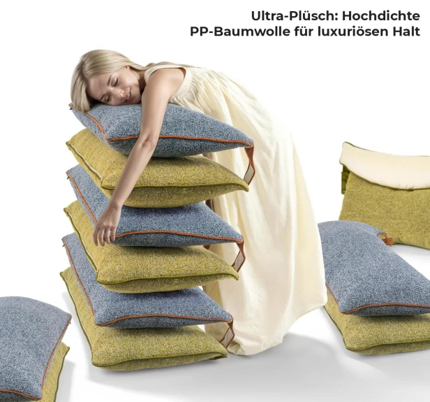 Eine junge, lächelnde Frau mit blonden Haaren, die ein langes, cremefarbenes Kleid trägt, bettet ihren Kopf auf einen hohen Kissenhaufen.