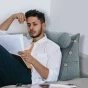 Mann lehnt an modularem Kopfteil mit Nackenrolle – graue Bettwäsche auf dem Bett.